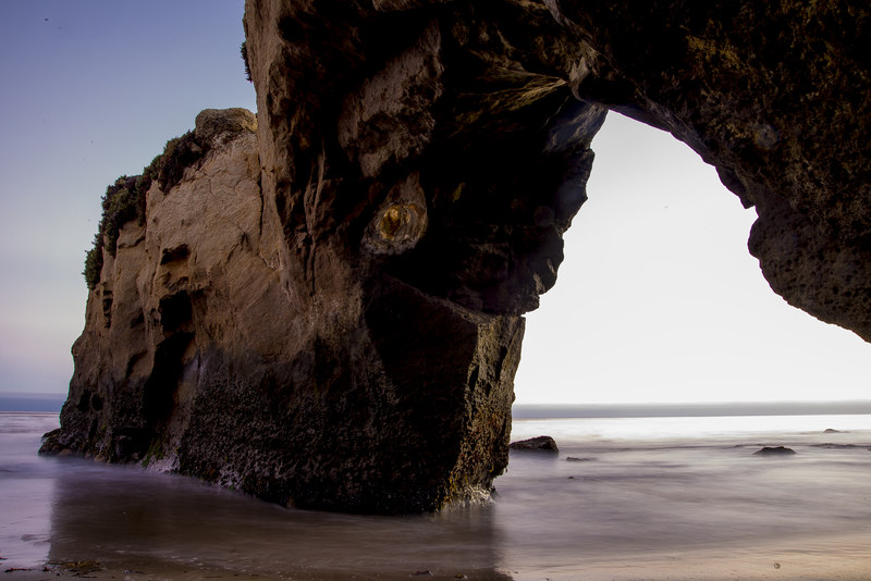 Dramatic coastal sea arch framing the ocean, long exposure silky water below at dusk